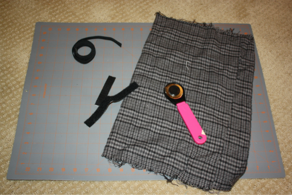 black elastic, black velcro strips, grey and black flannel material, fabric cutters, and a Fiskars quilting ruler to cut on.